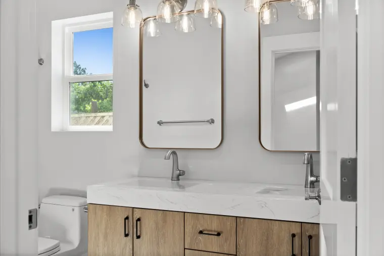 Double vanity in warm wood with a marble-look top, arched brass-framed mirrors, and globe pendant lights