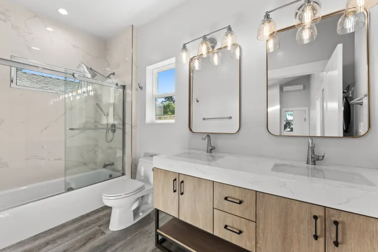 Bathroom with a glass-enclosed tub-shower in marble-look tile beside the double wood vanity