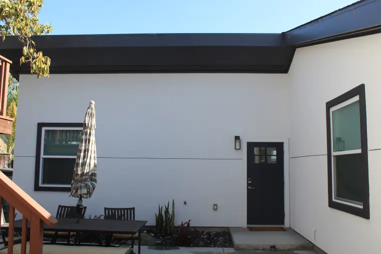 Side of the ADU with a black entry door, dark-framed windows, and a patio umbrella and dining set in front