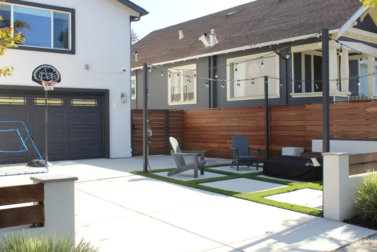 Front courtyard with concrete pavers set in turf, Adirondack chairs, string lights on black posts, and a horizontal wood fence
