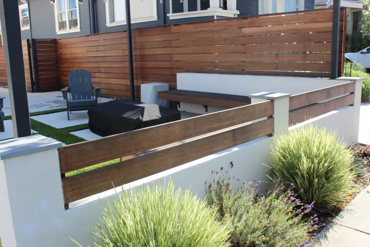 Stucco planter wall with wood rail cap and ornamental grasses in front of a courtyard with a horizontal wood fence