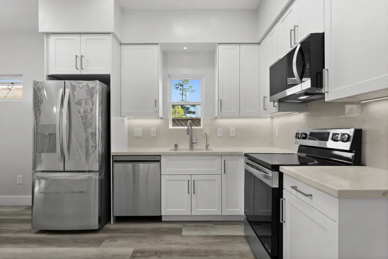 White shaker kitchen with stainless French-door refrigerator, electric range, quartz counters, and a window over the sink