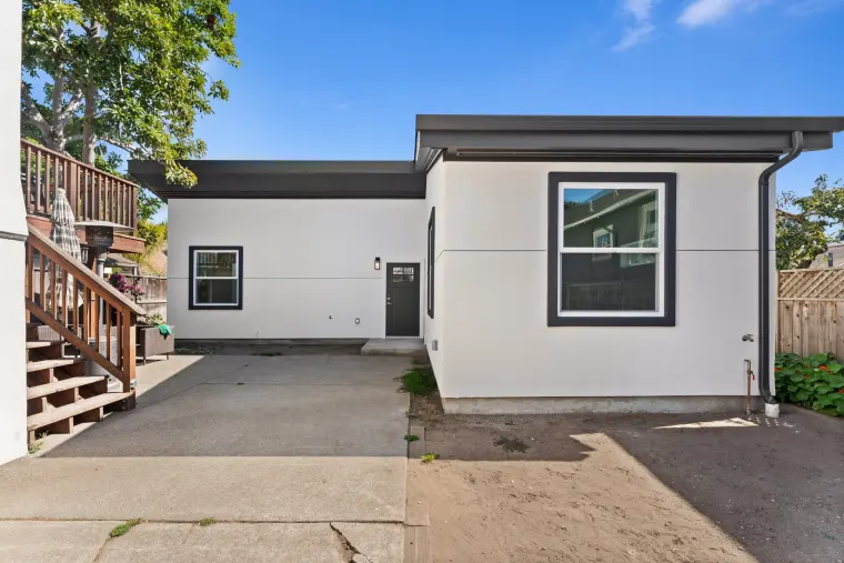 Finished ADU behind the main house: white stucco, black-trimmed windows, dark roof edge, and a concrete drive in front