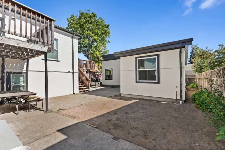 The ADU across the patio from the main house, with the raised wood deck and stairs and a picnic table between them