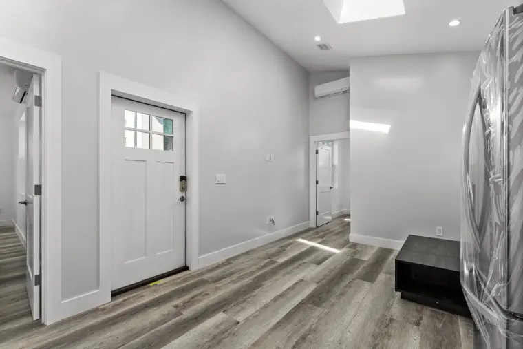 ADU entry from inside: white glass-paned front door, vaulted ceiling with skylight, and wood-look vinyl flooring