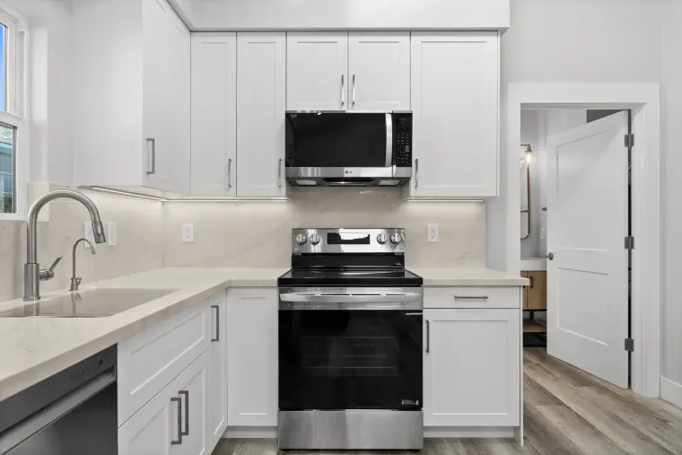 Kitchen corner with the sink, stainless range and microwave, marble-look backsplash, and a door through to the bathroom