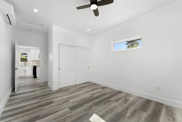 Bedroom with white sliding closet doors, ceiling fan, mini-split, and a clerestory window, door open to the living area