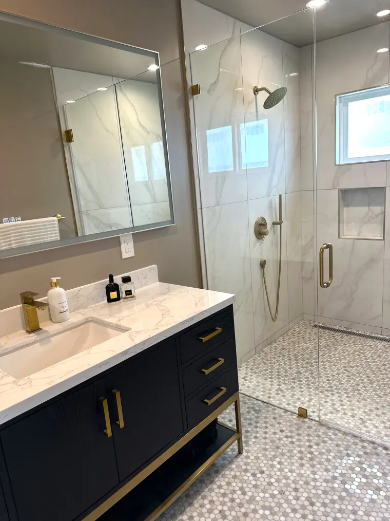 Bathroom with a navy vanity with brass legs and pulls, white counter, glass walk-in shower with brass fixtures, and hex mosaic floor