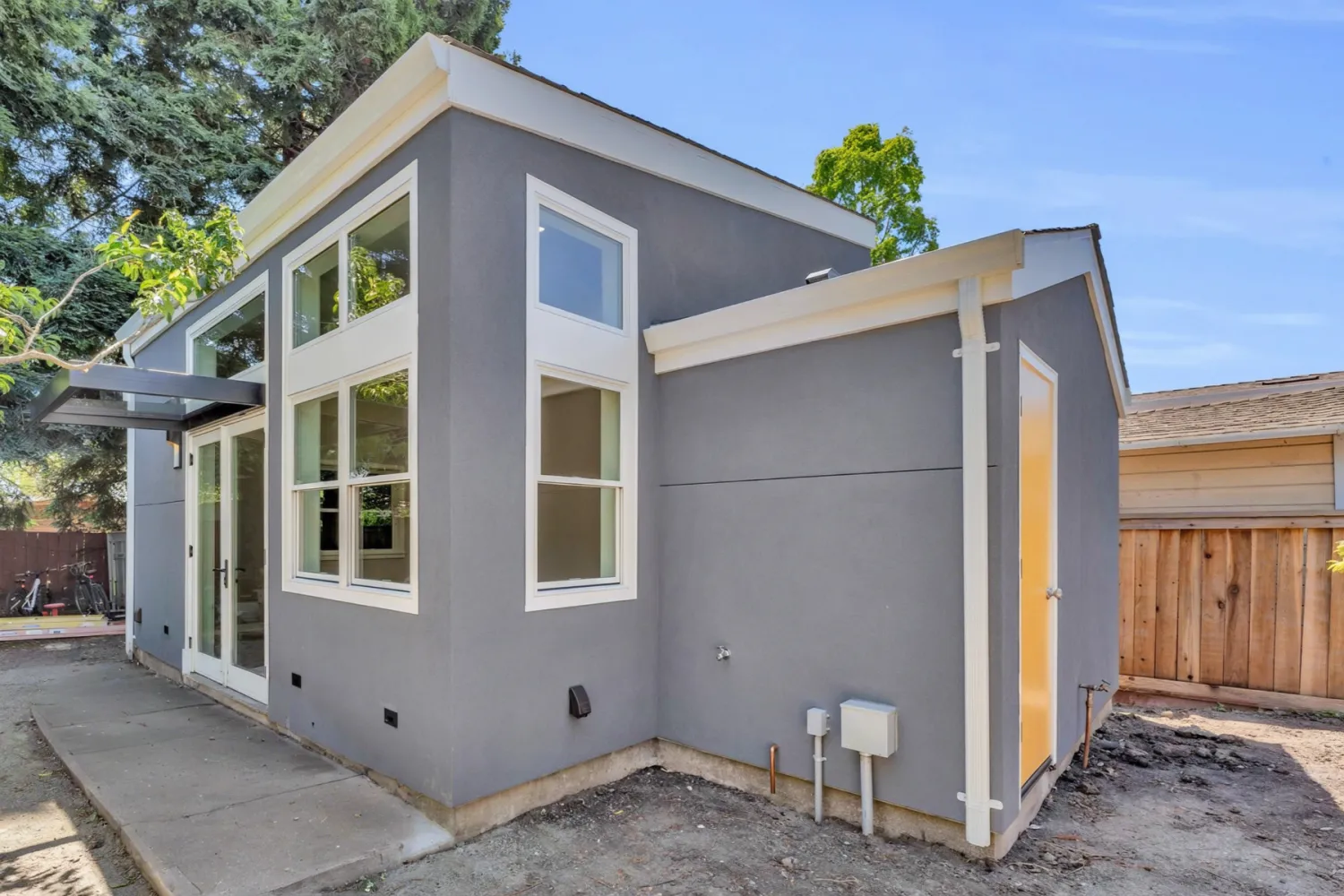 Finished gray ADU with white-trimmed windows, clerestories, and French doors, in a backyard setting