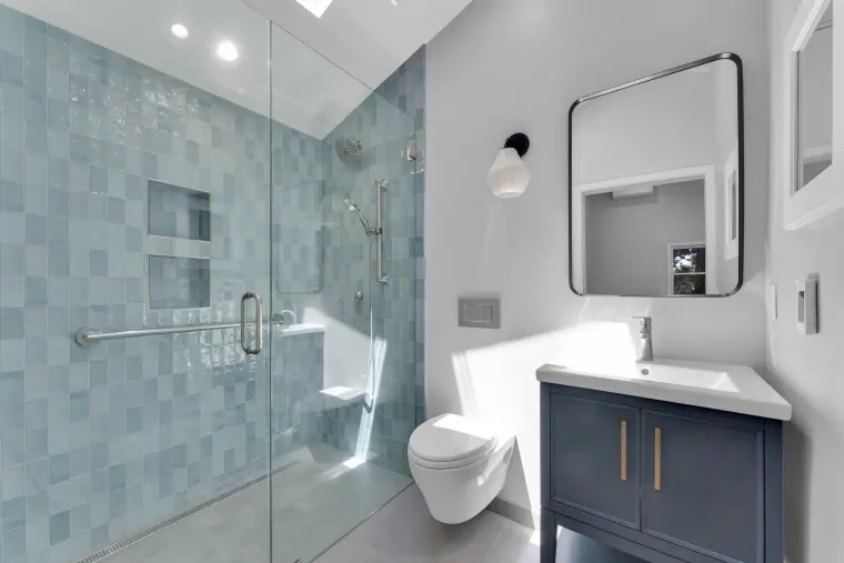 Bathroom with the blue-green tiled shower, wall-hung toilet, and a navy vanity with a black-framed mirror