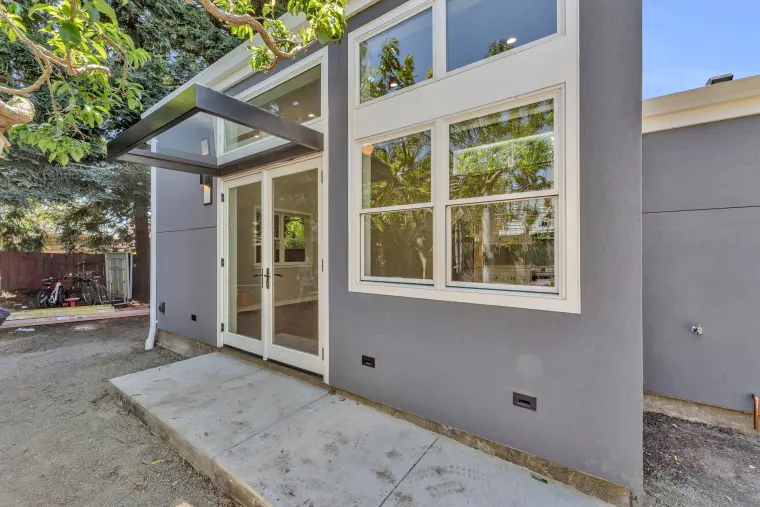 French doors under a black metal awning beside tall white-trimmed windows on the blue-gray stucco ADU