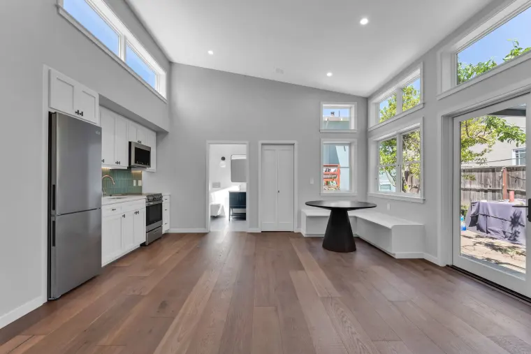 Studio interior with wide-plank oak floor, vaulted ceiling, kitchen wall on the left, and French doors and a dining nook at the far end