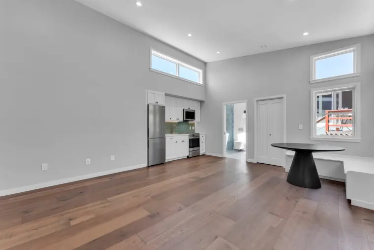 Vaulted studio with oak floor, a kitchen along the back wall, and a built-in bench nook with round black table under corner windows