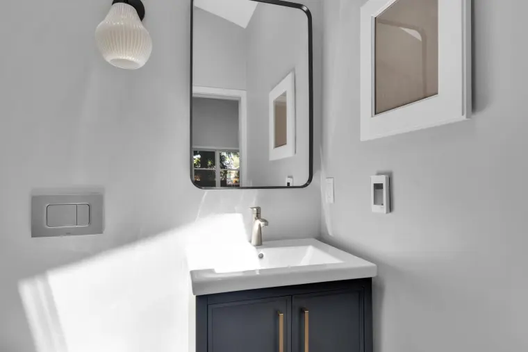 Floating navy vanity with white top, rounded black mirror, globe sconce, and wall-mounted flush plate