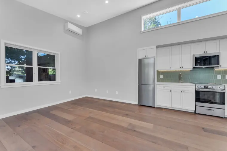 Living area looking toward the kitchen, with wide-plank floors and a mini-split