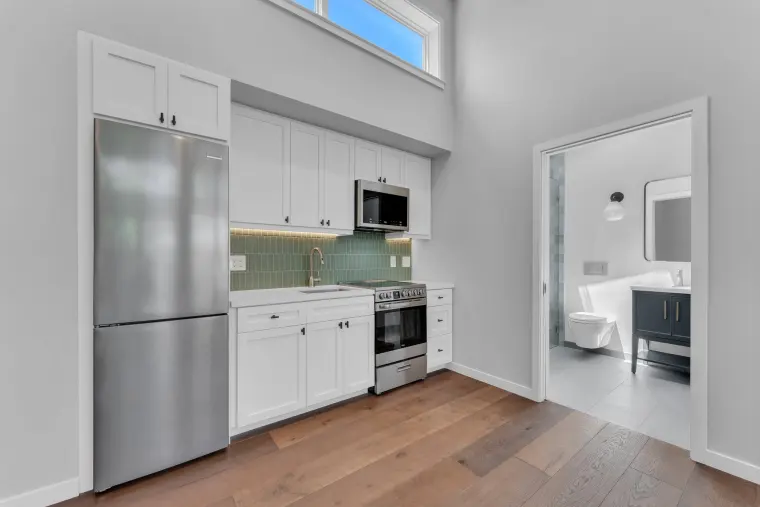 Kitchen wall with white cabinets, a stainless refrigerator and range, and a green tile backsplash
