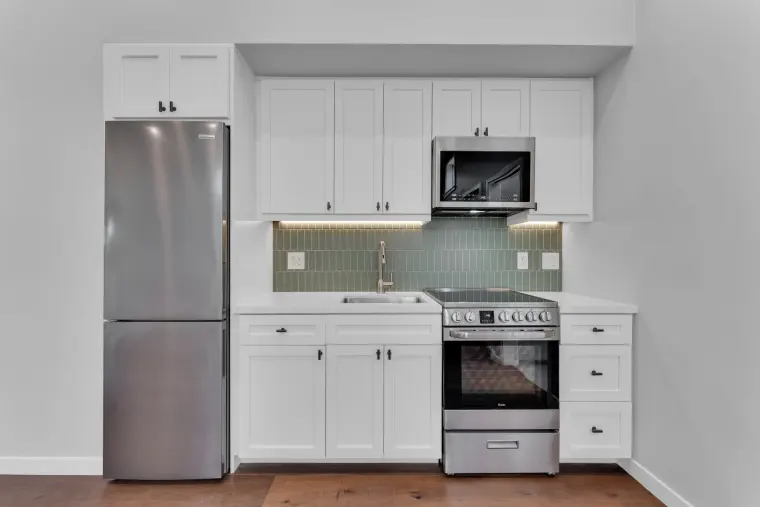 Compact kitchen with white shaker cabinets, green subway-tile backsplash, and stainless appliances