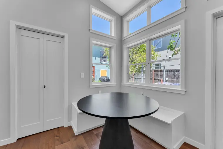 Dining nook with a round black table and window bench beneath corner windows