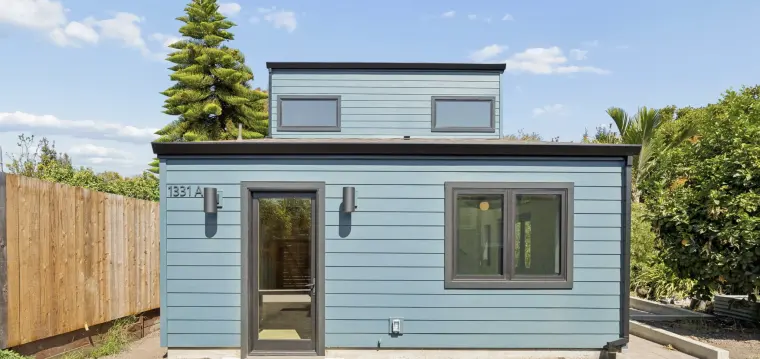 Two-story ADU in blue lap siding with black windows and a glass front door