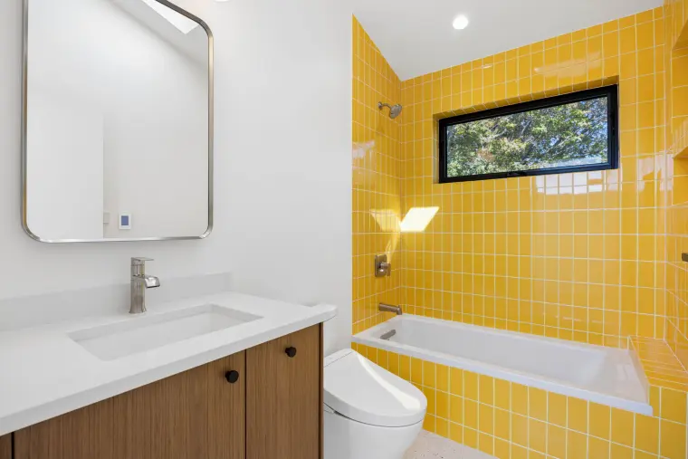 Bathroom with a bright yellow tile tub surround, oak vanity, and rounded mirror