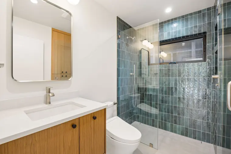 Second bathroom with an oak vanity and a glass shower in deep green tile