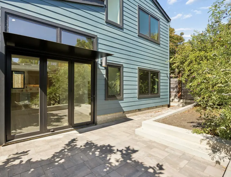 Back of the ADU with black French doors under a metal awning and a paver patio