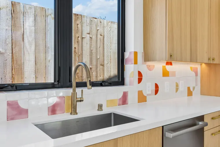 Sink under a black window with pink, orange, and red patterned tile