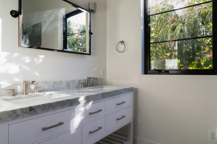 Bathroom vanity with a gray marble-look top, white drawers, and a black-framed mirror and window