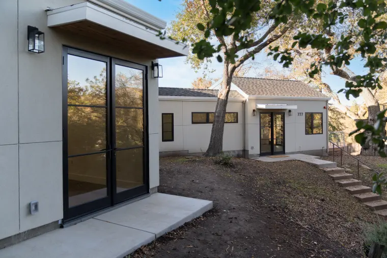 Black-framed sliding doors under a cantilevered canopy, the main house beyond