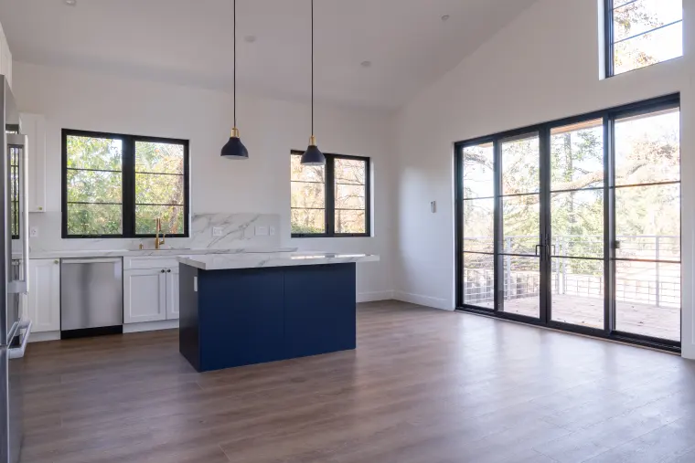 Open kitchen and living area with a navy island, black pendants, vaulted ceiling, and black-framed glass doors
