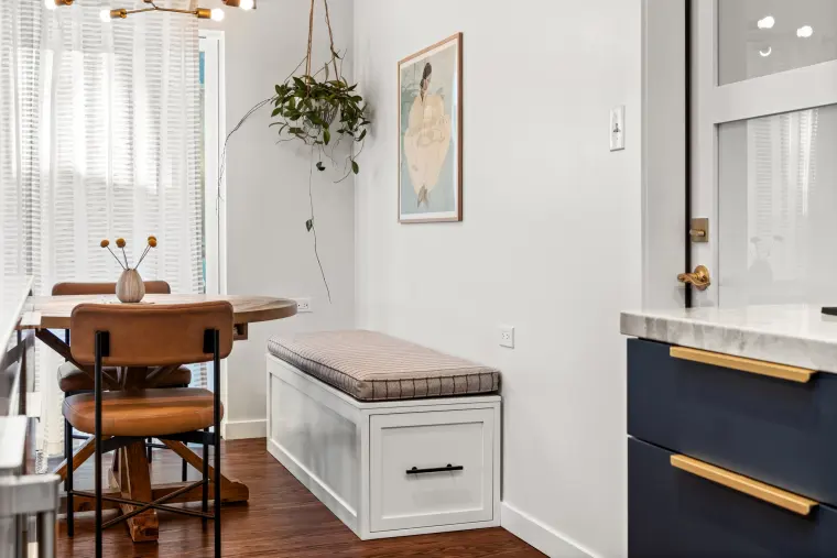 Built-in upholstered window bench with white base drawers beside the dining table and navy cabinets with brass pulls