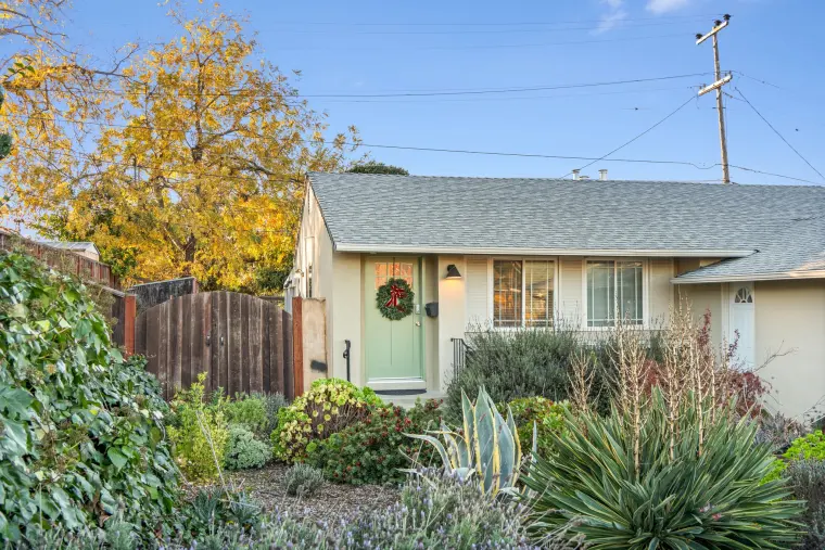 Single-story house with a green front door and wreath, wood fence, and drought-tolerant front yard landscaping under a blue sky