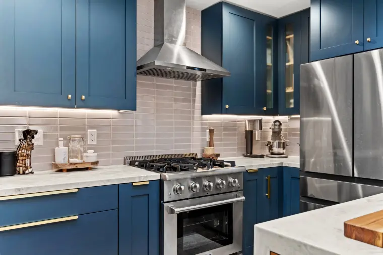 Navy cabinetry wall with a stainless gas range, chimney hood, gray stacked tile backsplash, and a stainless French-door refrigerator