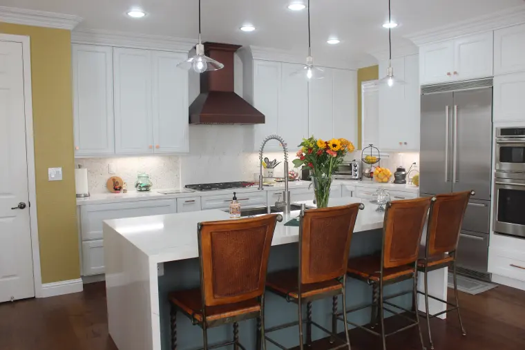 White kitchen with a dark range hood, a waterfall quartz island, and stainless appliances