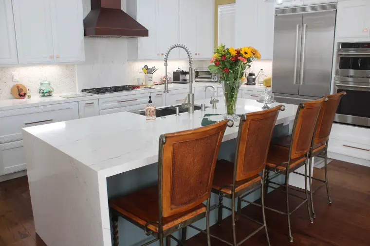 Waterfall island with seating for four, white cabinets, and built-in stainless ovens