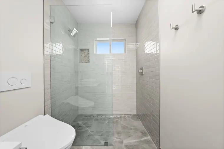Glass-enclosed shower with gray tile and a window above
