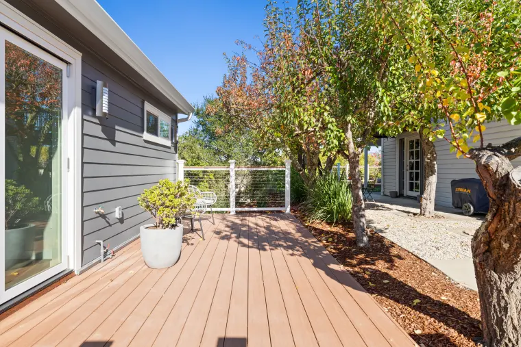 Composite deck along the gray ADU with a potted plant and cable railing, trees in fall color beyond