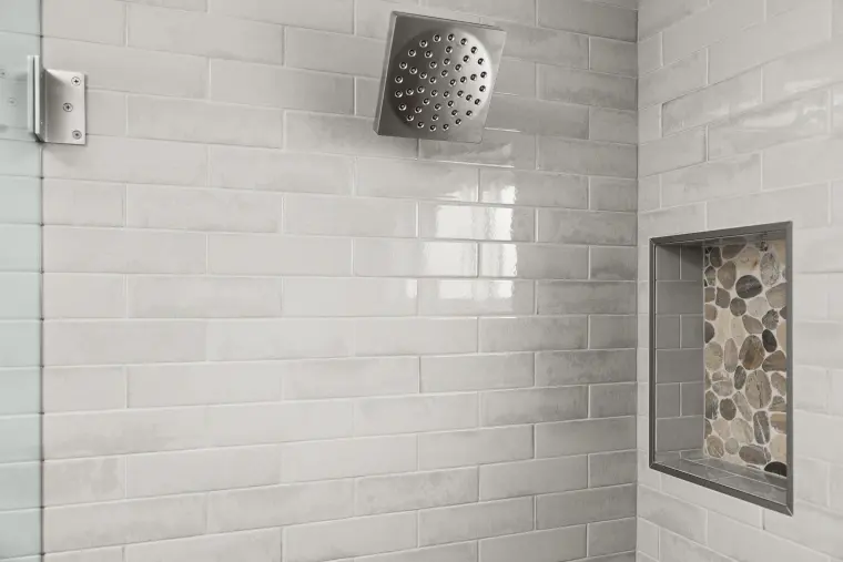Shower wall in glossy white subway tile with a square rain head and a pebble-lined niche