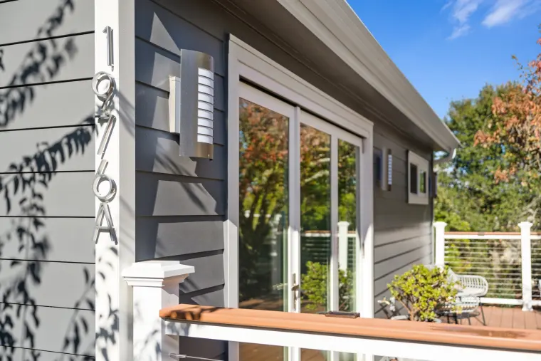 Gray lap siding with black-framed sliding doors opening onto the deck's white cable railing