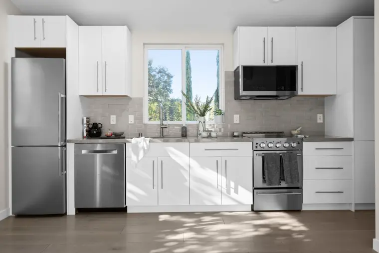 White kitchen with stainless refrigerator, range, and microwave, and a window over the sink
