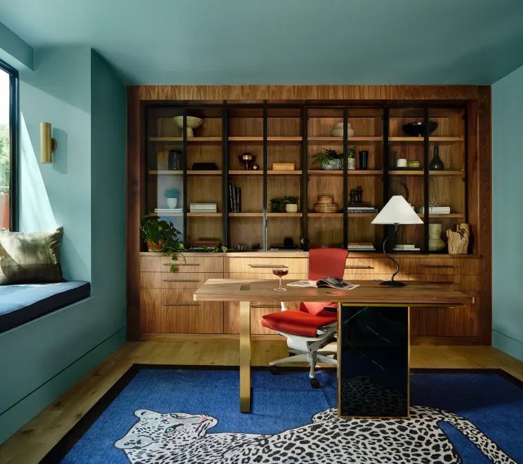 Home office with a teal wall of built-in wood shelving, a desk, and a patterned rug