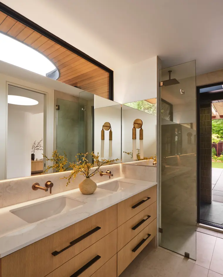Bathroom with a long wood vanity, round mirror, and cedar-lined skylight