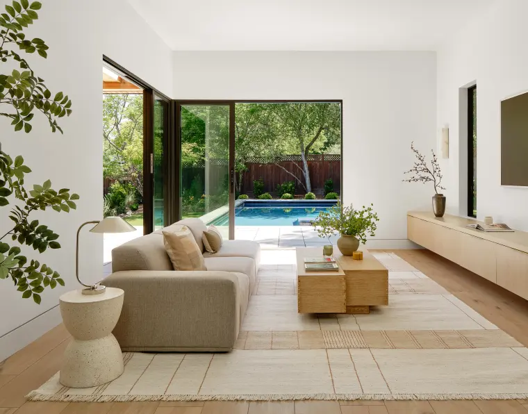 Living room with a low sectional, oak coffee tables, and a glass corner opening to the pool