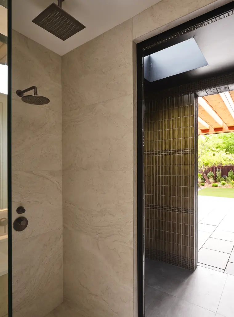 Shower with large-format stone tile and a rain head, its glass door open to a sunlit patio