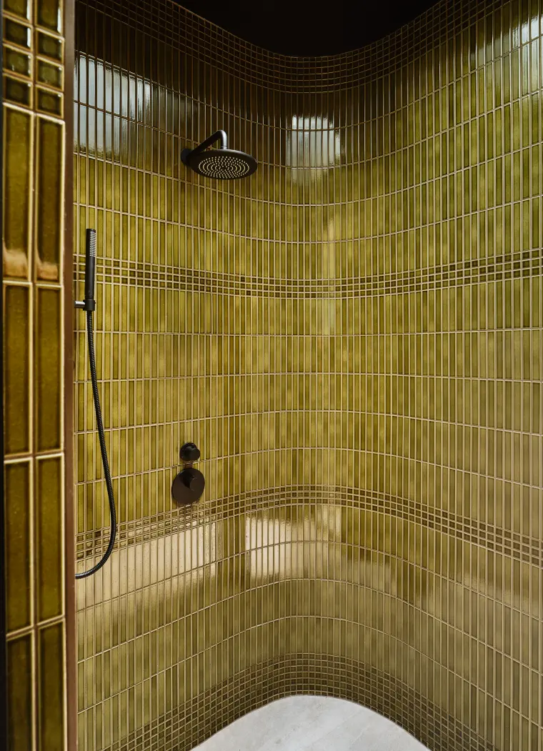 Curved shower wall in olive-green glazed tile with a black rain head and handheld sprayer