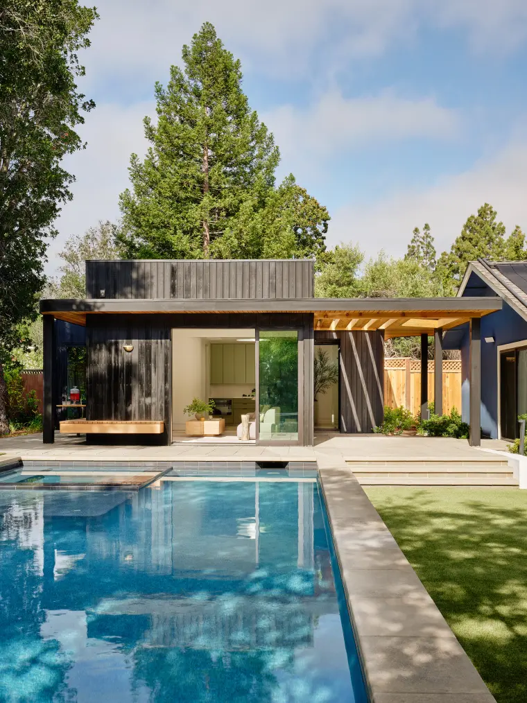 Charred-cedar ADU at the end of a pool, glass walls open to the water