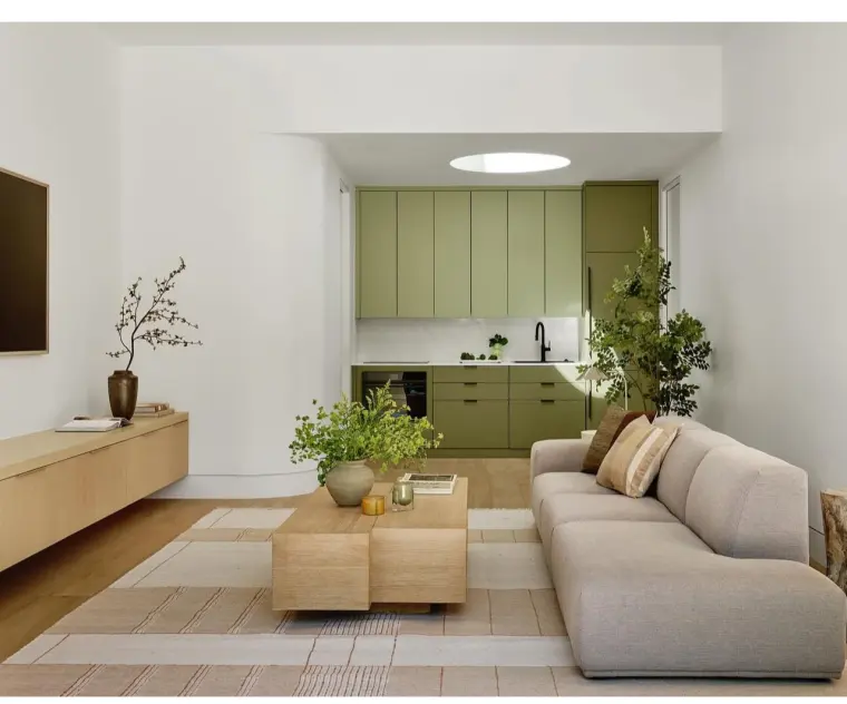 Living room with a low sectional, oak coffee tables, and a round skylight over the sage-green kitchen