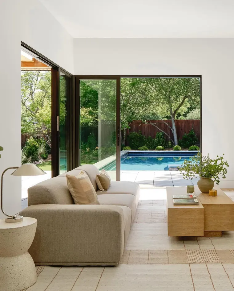 Sectional sofa beside a floor-to-ceiling glass corner opening to the pool