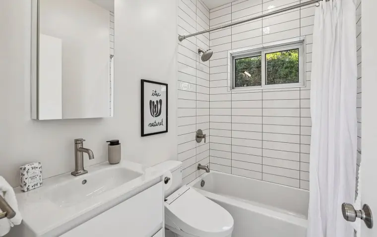 Bathroom with floating white vanity, white subway-tile tub surround with a window, and wall-hung toilet