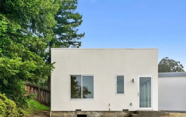 Side exterior of finished modern ADU with white stucco, sliding door entry, and view of neighboring property under blue sky